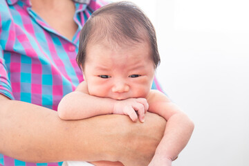 Wall Mural - Close up of Asian little newborn baby in her mother's arms, expressing warm loving caring feeling. Cute adorable baby hungry after wake up. Mom holding infant with safe and care.