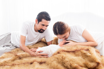 Wall Mural - Asian young mother father and newborn lying on brown wool blanket  together. Mom and dad looking adorable infant with love and tender, Little baby deeply sleeping wrapped in thin white cloth.