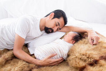 Wall Mural - Selective focus of Father Sleeping with newborn baby in bed. Asian little baby lying wrapped in thin white cloth on brown wool. Dad sleeping and touch adorable toddler with love and care.