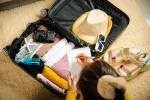 Making Check List Of Things To Pack For Travel. Woman Writing Paper Take Note And Packing Suitcase To Vacation Writing Paper List Sitting On Room, Prepare Clothes Into Luggage, Travel Vacation Travel