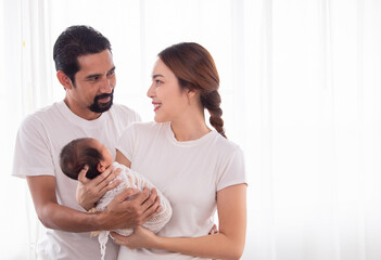 Wall Mural - Selective focus of Asian woman and man holding newborn baby at home. Happy family smiling with adorable infant spend time together, young parents holding little toddler, love and happiness concept.