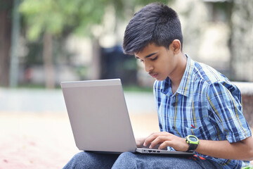 Wall Mural - Indian young boy using Laptop while Sitting Outside park	
