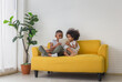 © iPoguz - Sister and brother playing togetherness fun in living room, Two little kids siblings seated on sofa using tablet smartphone and book