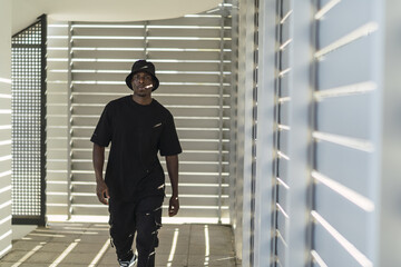 Wall Mural - Young cool black male in a street style outfit posing in a room with blinds