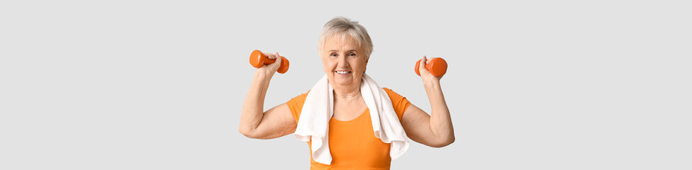 Wall Mural - Elderly woman holding dumbbells on light background with space for text