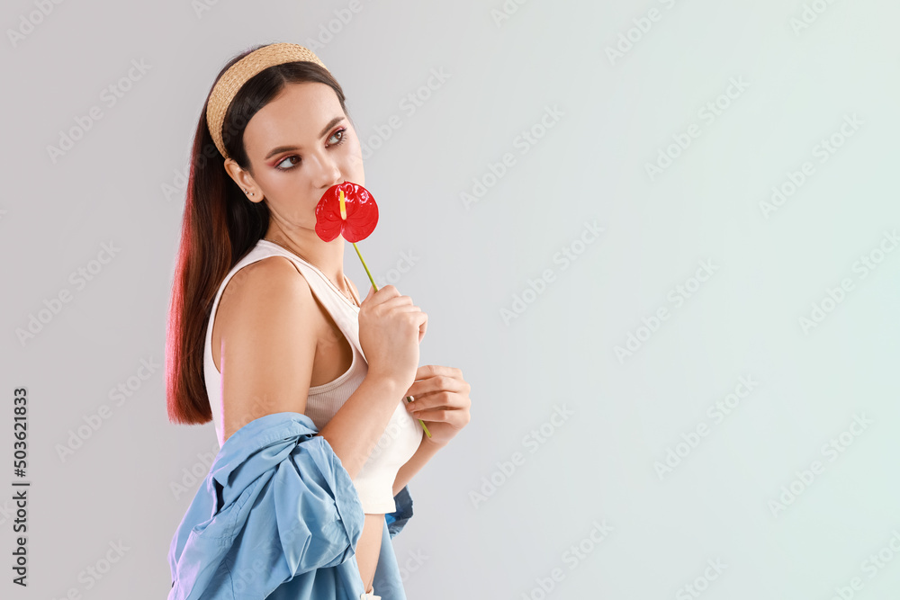 Beautiful woman smelling anthurium flower on light background