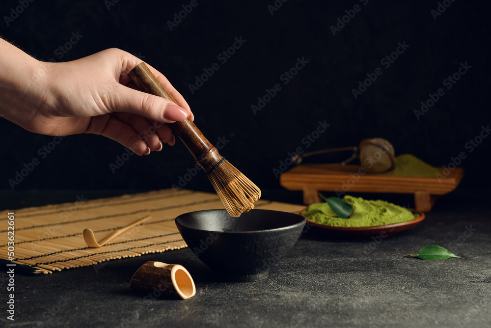 Woman preparing tasty matcha tea on dark background, closeup