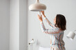 © Pixel-Shot - Woman changing light bulb in hanging lamp at home