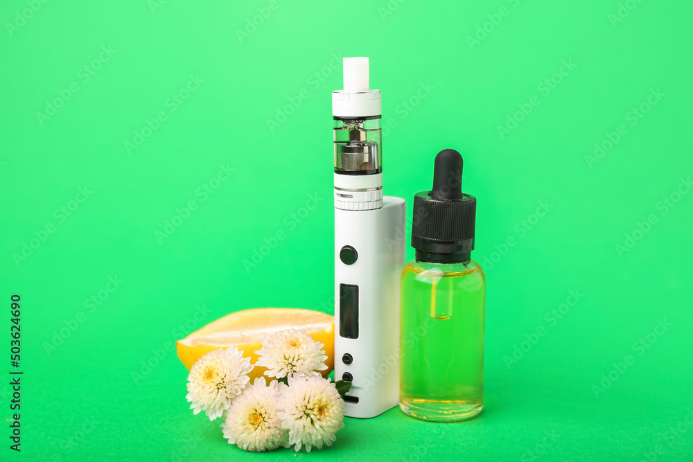 Modern vape mod, oil, lemon and flowers on green background