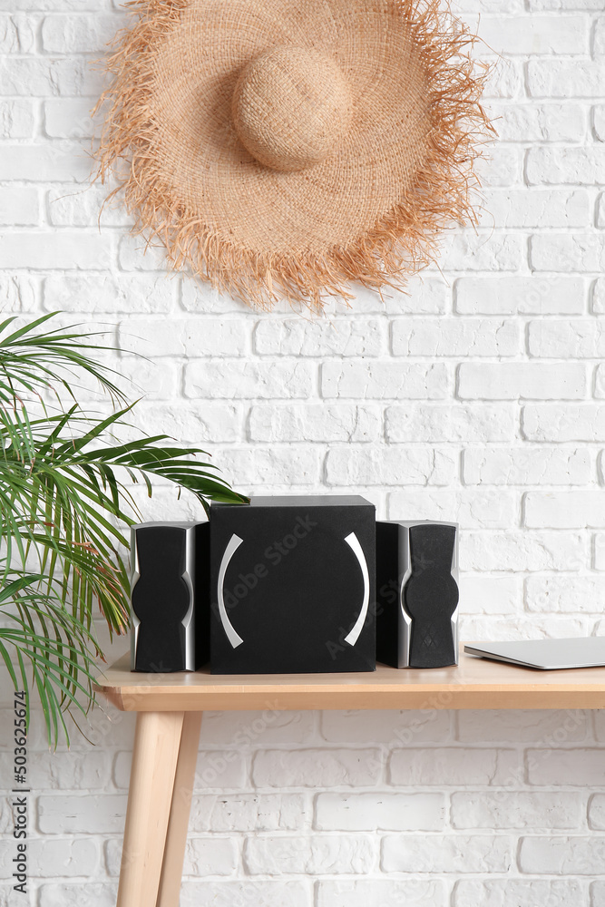 Modern speakers and laptop on table near white brick wall