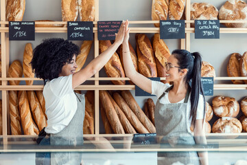 Couple women owners bakery working while celebrating by high fives monthly earnings in a pastry shop.