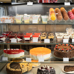 Many colorful delicious pastries and cakes in a glass showcase in a pastry shop close-up. Appetizing pastel sweet desserts on display with cream filling.