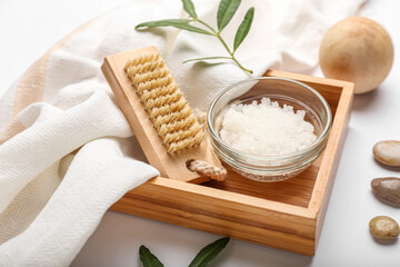 Wooden box with bowl of sea salt and massage brush on white background, closeup