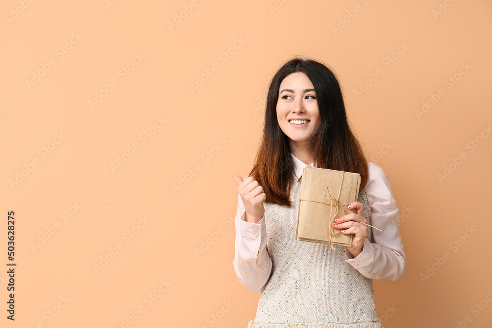 Young Asian woman with stack of invitations pointing at something on beige background