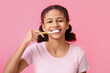 African-American teenage girl brushing teeth on pink background