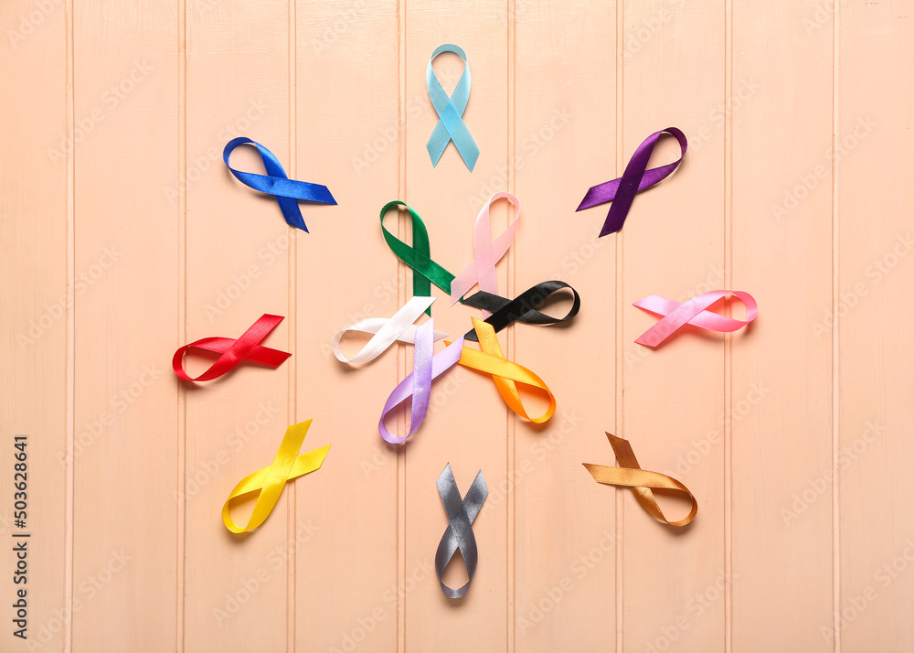 Different awareness ribbons on color wooden background. World Cancer Day concept