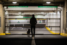 Back View Of A Person With His Dog  In Front Of Car Park In Downtown Vancouver, Canada