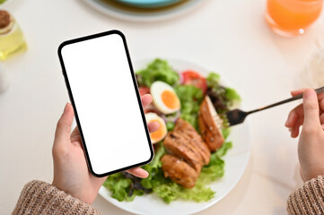 female using smartphone while eating healthy organic grilled chicken salad.