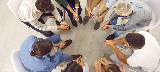 Wall Mural - People talking in group therapy session or community meeting. Team of young and mature men and women sitting in circle and having serious discussion. High angle shot, top view banner background