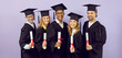 © Studio Romantic - Happy diverse mixed race multi ethnic male and female university students in graduate hats and robes smile at camera and show paper diploma scrolls standing on purple background at graduation event