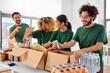 © Syda Productions - charity, donation and volunteering concept - international group of happy smiling volunteers packing food in boxes according to list on clipboard at distribution or refugee assistance center