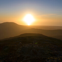 Wall Mural - A man standing on a mountain summit stone at sunset