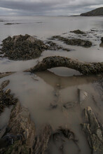 A Muddy British Beach Scene With Driftwood And Seaweed