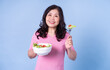 © Timeimage - Image of middle aged Asian woman eating salad on blue background