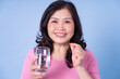 © Timeimage - Image of middle aged Asian woman using pill on blue background