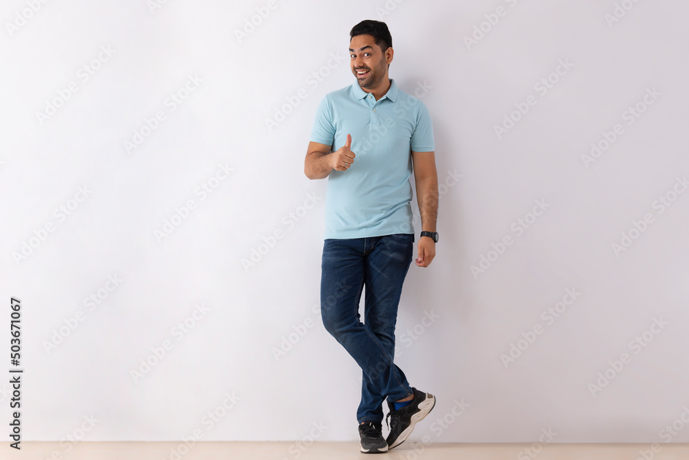 Portrait of a young man showing thumb while standing against white ...