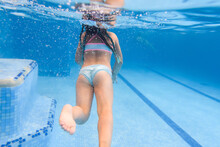 Kid girl swimming underwater in the paddling pool. Diving. Learning child to swim. Enjoy swims and bubbles. Back view.