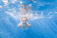 Little Child Girl Swimming Underwater In The Paddling Pool. Diving. Learning Infant Child To Swim. Enjoy Swimming And Bubbles.