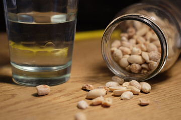 Closeup of spilled peanuts from a jar and a glass of water on the side