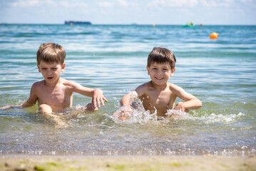 Wall Mural - Happy family playing in blue water of swimming pool on a tropical resort at the sea. Summer vacations concept. Two brother kids are best friends