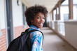 Portrait of smiling african american elementary schoolboy looking over shoulder in school corridor