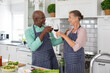 Happy senior multiracial couple toasting red wine while standing in kitchen at home