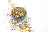 Fototapeta Mapy - Cup filled with dry herbs on scattered herbal leaves on white background,copy space for text.