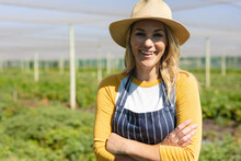 Portrait Of Smiling Caucasian Mid Adult Female Farmer Wearing Hat With Arms Crossed In Greenhouse