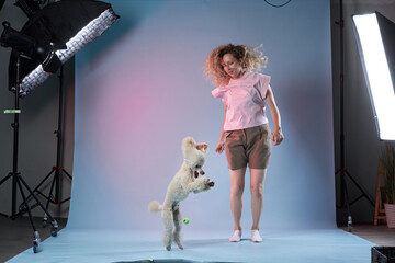 Wall Mural - happy girl with a dog jumps, plays in a photo studio on a bright colored background. Poodle and curly woman