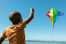 African American Boy Enjoying Kite Flying Against Blue Sky On Sunny Day