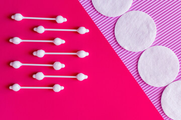 Wall Mural - flat lay of ear sticks and cotton pads on pink and violet textured background, top view.