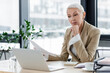 © LIGHTFIELD STUDIOS - senior financier holding documents while sitting near laptop.