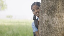 Smiling girl kid peeking behind the tree in school uniform - concept of education, shy and freedom.