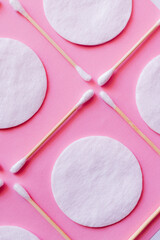 Wall Mural - close up of ear sticks and cotton pads on pink background, top view.