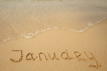 Wall Mural - January - drawing on the soft beach sand with a soft lapping wave.