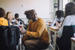 © Maskot - Side view of male teacher talking with student while crouching amidst desks in classroom