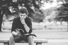 Closeup Of A Man Reading A Book And Sitting On A Bench In A Park
