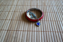 Closeup shot of a red bracelet and necklace with a blue heart on a wooden surface