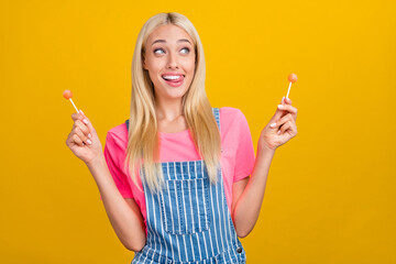 Sticker - Portrait of attractive cheerful girly cute girl eating candies having fun licking lip isolated over bright yellow color background