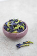 A handful of dried butterfly pea flowers in small cup on a white stone background. Blue flower for tea.